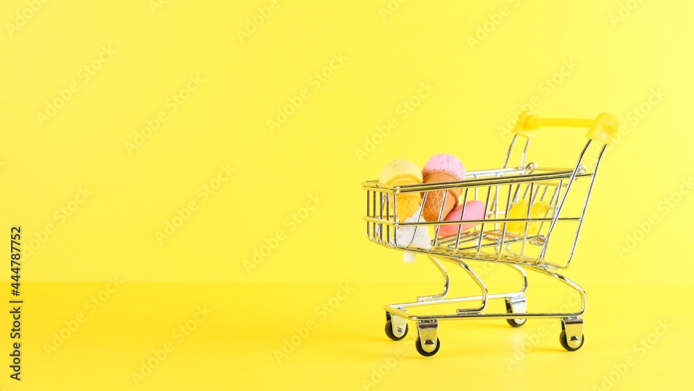 Shopping cart with ice cream inside on a yellow background, closeup. Black Friday Shopping and Discount Concept.