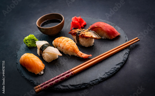 Beautifil composition of sushi sashimi set with shrimps, ginger and soy sauce served with chopsticks and green wasabi on black round plate. Traditional japanese food with rice and seafood