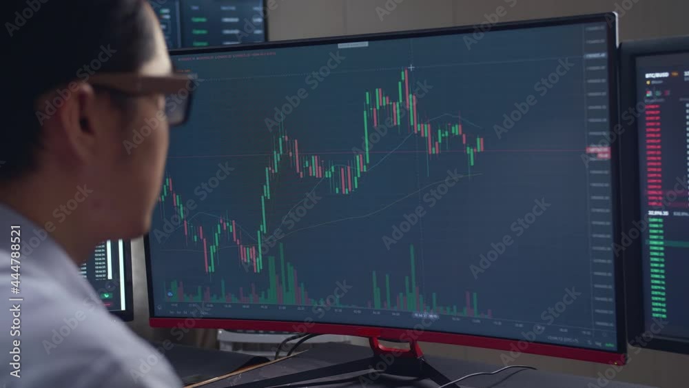 Asian Male Stock Market Broker Looking Analyzing Graphs On Multiple Computer Screens 
