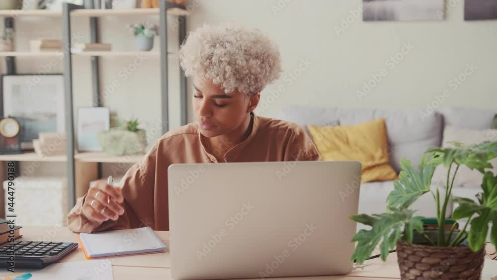 Young African American woman with many debts feeling stressed calculating finances, sitting at home office table with papers laptop making calculations on calculator, trying to make both ends meet. Young African American woman with many debts feeling stressed calculating finances, sitting at home office table with papers laptop making calculations on calculator, trying to make both ends meet.