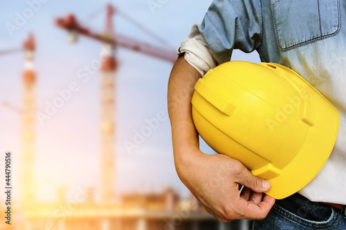 Hand's engineer worker holding yellow safety helmet with building on construction site background