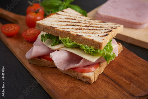 Sandwich with ham and cheese. Grilled and pressed toast with smoked ham, cheese, tomato and lettuce served on wooden cutting board. Cafe - Sandwich with bacon, cheese, ham and vegetables.
