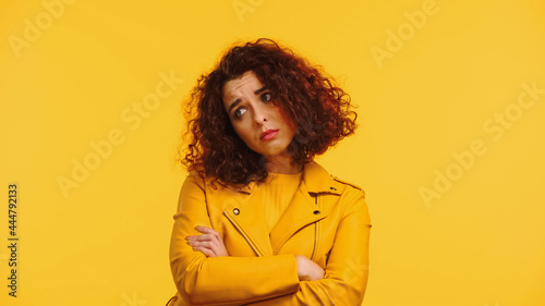 upset young woman in leather jacket standing with crossed arms isolated on yellow © LIGHTFIELD STUDIOS