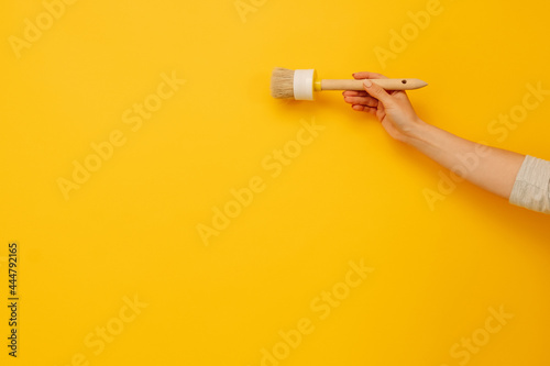 Woman hand holding wooden paint brush on yellow background with copy space. Concept of creativity, improvement and inspiration. Working tool for home design project