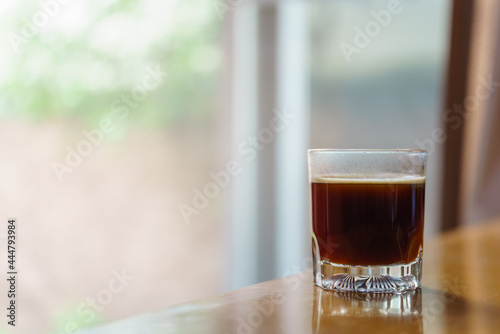 Closeup of glass of hot black coffee Americano with sunlingt and shadow on wooden table with copy space. photo