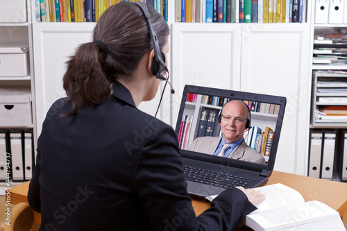 Woman with headset in front of her laptop and a book making an online phone call with a client or colleague, copy space