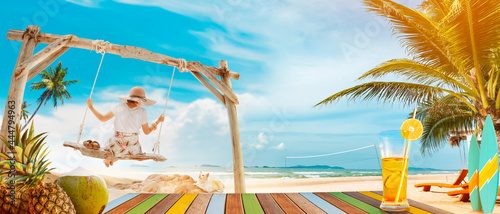 Back view of woman swinging on a swing on white sandy beach in tropical destination. Enjoying the amazing view of blue sea and tropical fruits on a sunny day. Girl relaxing on exotic summer holiday.