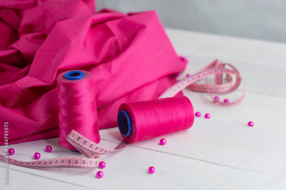 Pink satin fabric with thread and centimeter on wooden background with beads. Pink satin fabric with thread and centimeter on wooden background with beads.
