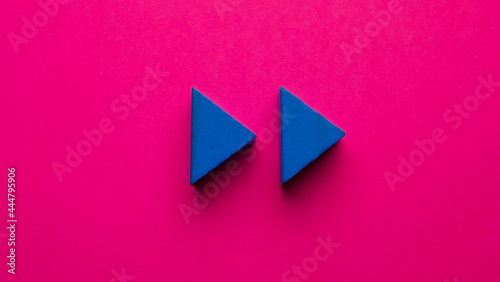 
blue wooden triangles simulating rewind symbol on pink background photo