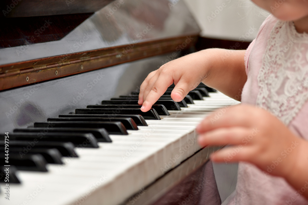 A little girl presses her fingers on the white keys of the piano. Teaching children at a music school.