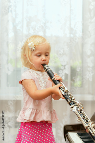 A little girl blows the clarinet and closes the chord switching holes with her fingers.