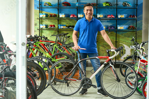 Handsome positive sales assistant standing in store next to bicycle he is selling