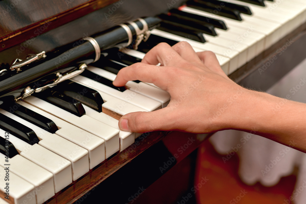 Fototapeta premium The clarinet lies on the black piano keys, the musician takes a chord on the white keys.