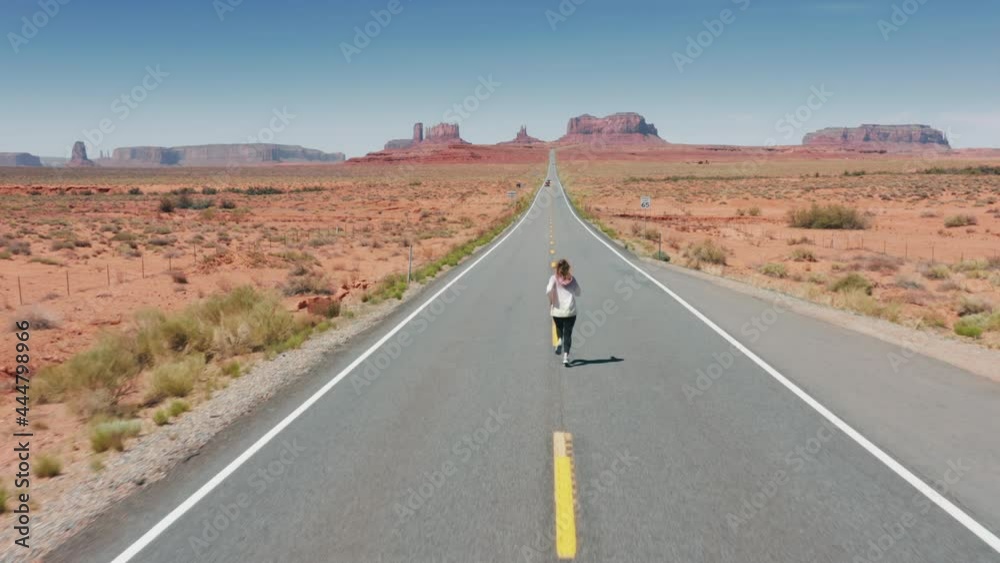 Cinematic aerial athletic woman running by highway to Monument Valley, nature 4K