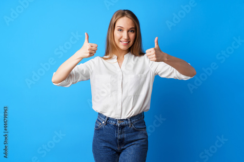 Young blonde woman showing thumbs up sign against blue background