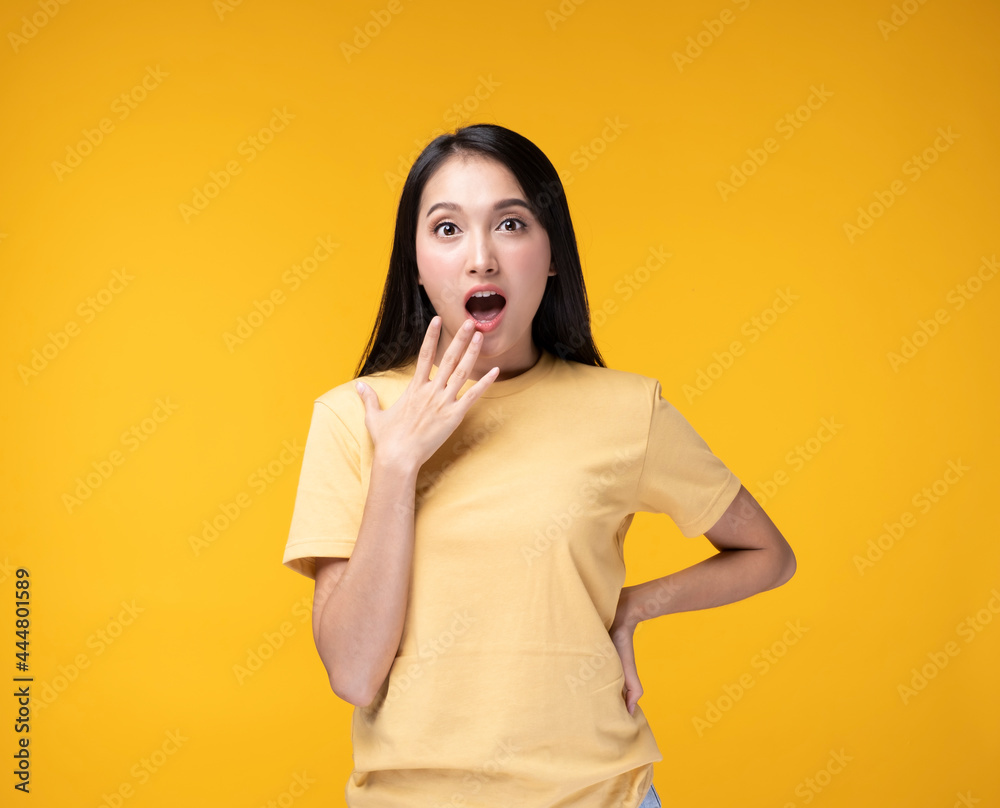 Young Asian woman making hand gesture with surprise face. Happy Asian woman wearing yellow t-shirt standing over yellow background. Portrait of happy Asian female .