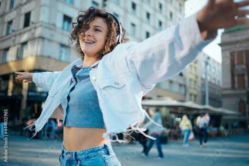 Young happy girl with curly hair dancing on the street and listening music.