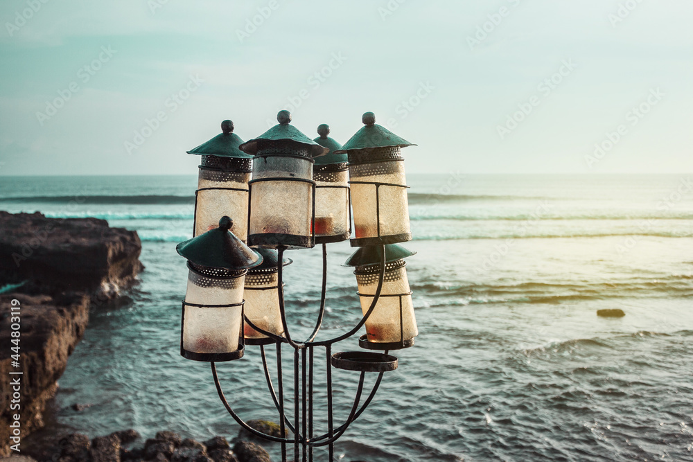 A outside lamps (lanterns) in the candlestick with candles on the ocean and cliffs background. Romantic sunset on the sea (ocean) coast. Bali, Indonesia. Echo beach. Canggu.