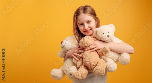 Obraz na płótnie Cute girl child hugging three teddy bears isolated on yellow background with copyspace