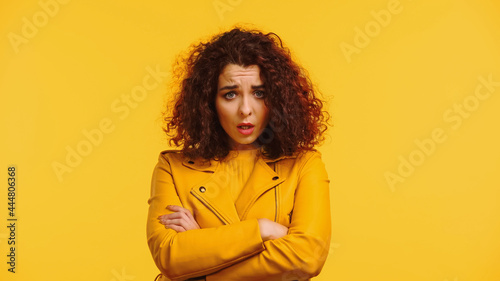 offended woman in leather jacket standing with crossed arms isolated on yellow © LIGHTFIELD STUDIOS