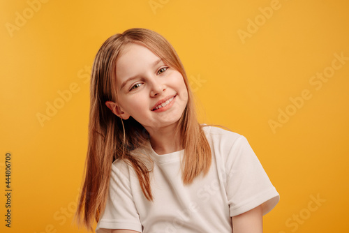 Beautiful little girl looking at the camera and smiling isolated on yellow background with copyspace. Cute teen kid portrait