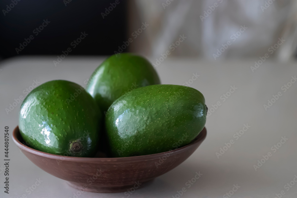 Green avocado in a brown plate on a light background. Green avocado in a brown plate on a light background.