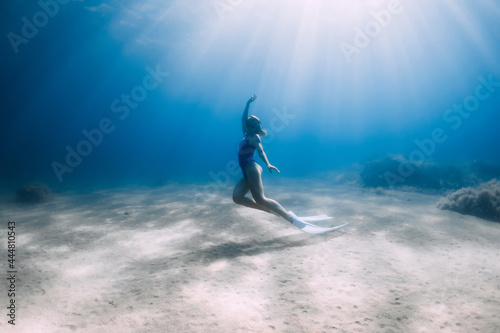 Lady free diver in swimsuit posing underwater at the deep in blue sea with sunlight.