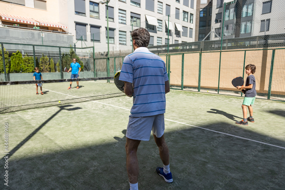 paddle match between two adults and two children on the paddle court of their residential complex.