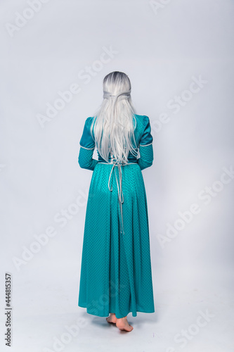 Full length portrait of a standing back princess in a medieval, fantasy, turquoise dress with ash hair and a silver crown posing isolated on a white background.