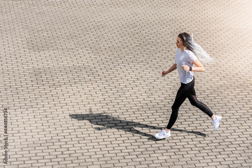 Woman listening music running in city street. Sport activities on street and music