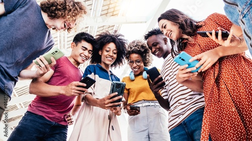 Diverse teenage students using digital smart mobile phones on college campus - Group of friends watching cellphones sharing content on social media platform - Youth, friendship and technology concept	