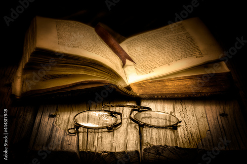 Libro antiguo abierto con una cinta separadora y con un binocular sobre la mesa en un primer plano
