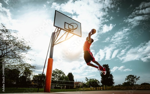 Street basketball player making a powerful slam dunk on the court - Athletic male training outdoor at sunset - Sport and competition concept	
 photo