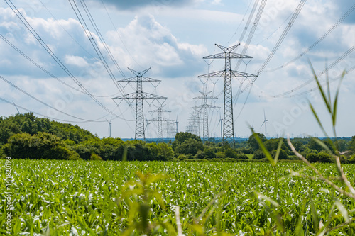 Towers with multiple power lines over a green field with blue sky