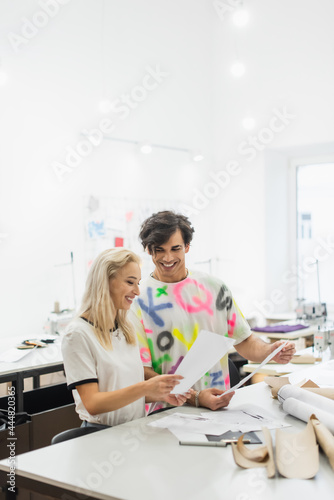 happy fashion designers holding papers while working in tailor shop
