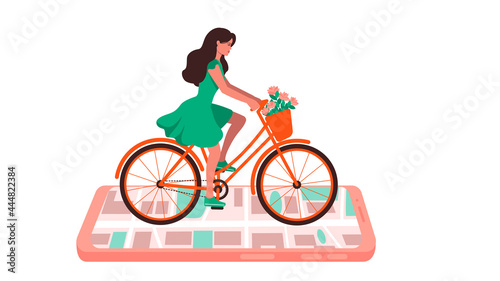 A girl in a green dress is riding a bicycle on a smartphone with a city map . There are flowers in the basket of the bike .