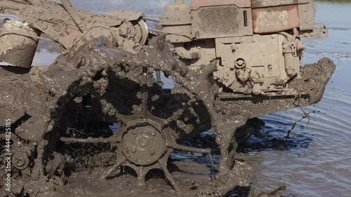 A close up of splashes of mud on a grouser of a tilling machine. Slow motion footage of a plougher equipment on a farm. Taming soil before seeding. RIce field agricultural industry. Spring labour. photo