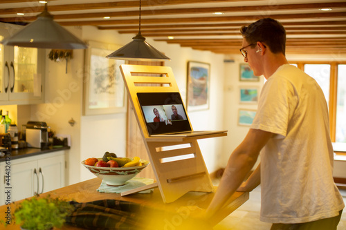 Man video conferencing at laptop stand desk in kitchen photo