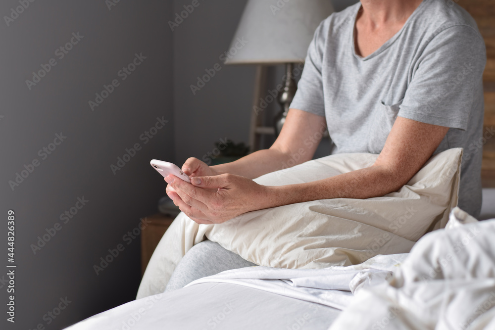 Obraz premium Woman is using mobile phone sitting on her bed with a pillow