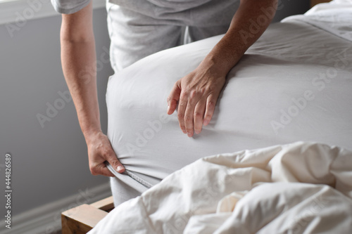 Woman is putting on a fitted sheet on a mattress while making the bed photo