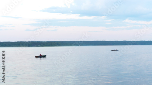 A fisherman on his fishing boat on a calm river at sunset. Warm beautiful summer evening.
