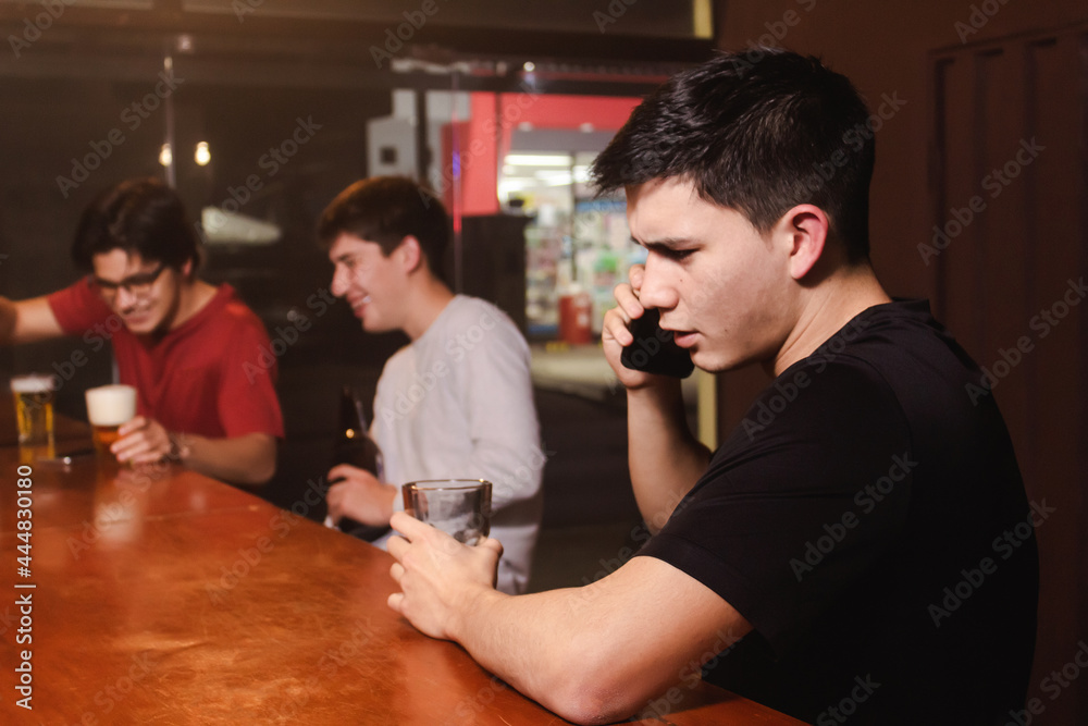 An angry young man talking on the phone while his friends enjoy a beer and laugh at the bar. An angry young man talking on the phone while his friends enjoy a beer and laugh at the bar.