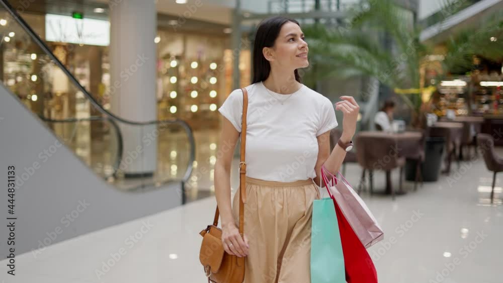 Happy caucasian woman in stylish outfit with happy face expression smiling while looking around modern big mall, holding bunch of paper bags and enjoying seasonal shopping Happy caucasian woman in stylish outfit with happy face expression smiling while looking around modern big mall, holding bunch of paper bags and enjoying seasonal shopping