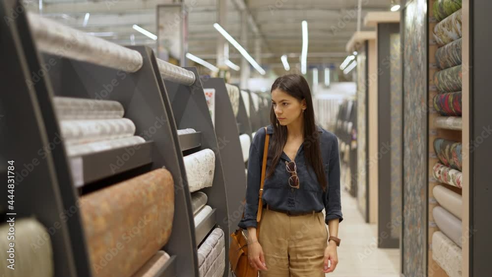 Young female customer looking at large assortment of wallpapers for home interior design in construction department of shopping mall, woman choosing materials for repairing her room Young female customer looking at large assortment of wallpapers for home interior design in construction department of shopping mall, woman choosing materials for repairing her room