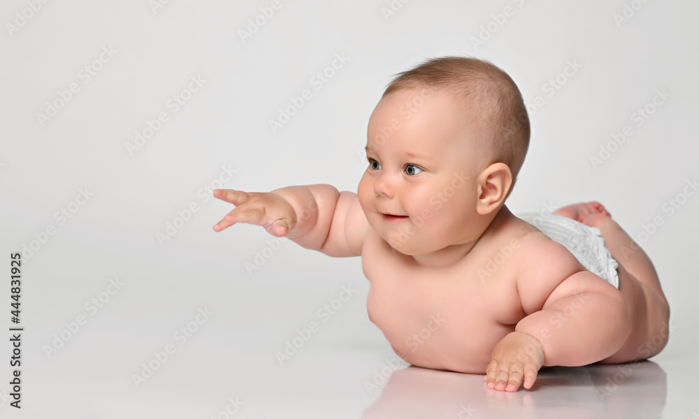 baby infant lies on his stomach in one diaper and tries to talk to someone, pulls his chubby hand to the side. on a set background. baby infant lies on his stomach in one diaper and tries to talk to someone, pulls his chubby hand to the side. on a set background.