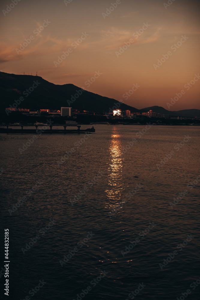 Evening view of the city with the sea horizon, mountains and orange sunset. Vertical