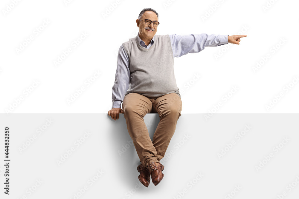 Mature smiling man sitting on a blank panel and pointing to the side Mature smiling man sitting on a blank panel and pointing to the side