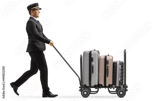 Full length profile shot of a bellboy walking and pushing a trolley cart with suitcases photo