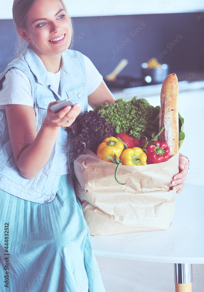 Young woman holding grocery shopping bag with vegetables .Standing in the kitchen Young woman holding grocery shopping bag with vegetables .Standing in the kitchen