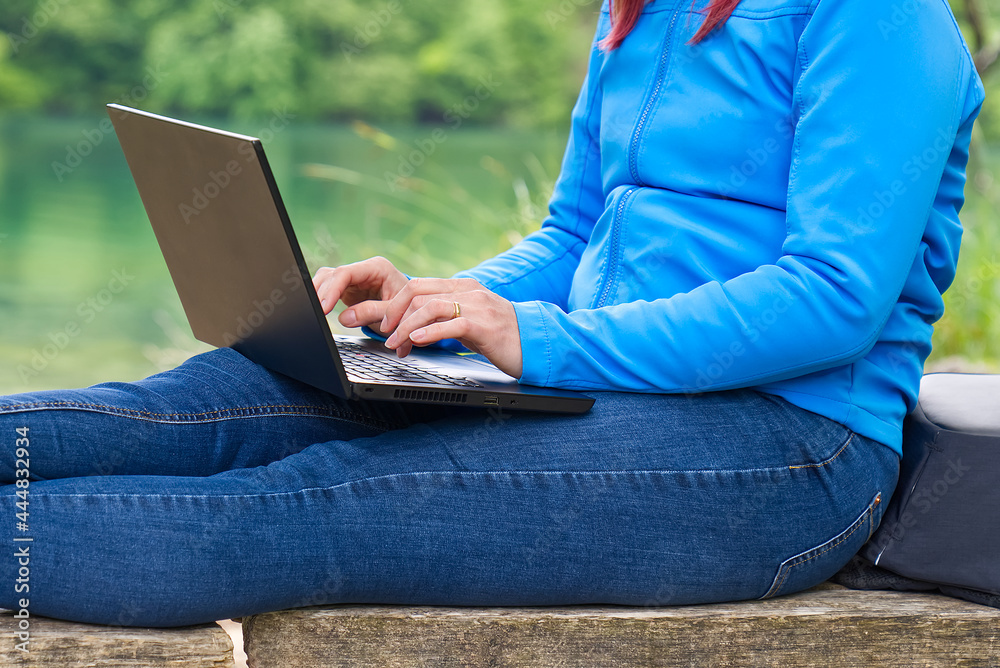 Naklejka premium Work from anywhere. Remote freelancer work in nature. Young woman, female freelancer working with laptop with Beautiful view of forest and lake. freelancer paradise, freedom of teleworking. distance
